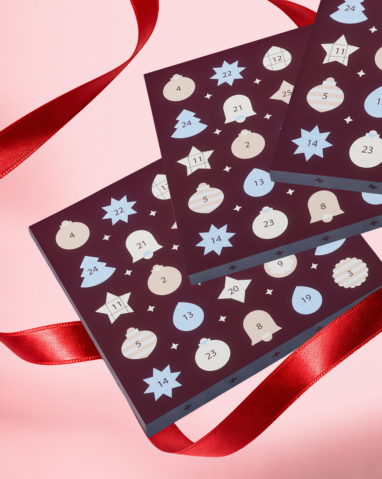 Two dark purple advent calendar boxes with star- and circle-shaped windows, tied with red ribbons on a pink background.